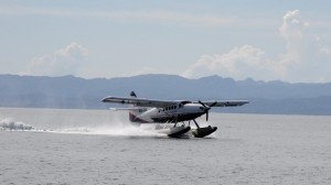 Ein Wasserflugzeug landet und faehrt kurz danach quer durch den Ankerplatz zum Steg des Ressorts.